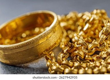 Närbild på en guldring och en guldkedja på en mörk yta.
